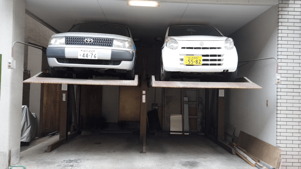 Minimal parkering under bostadshus i Osaka 2019. En keibil med gul nummerplåt till höger och en ”vanlig” småbil till vänster med vit nummerplåt. Foto: Pelle Sten